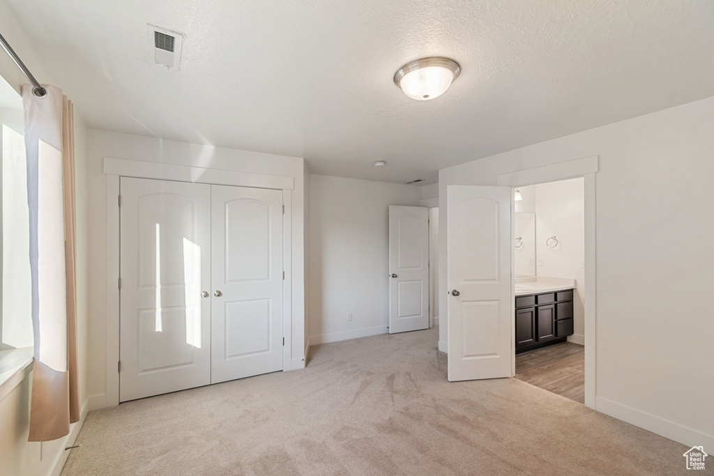Unfurnished bedroom featuring light colored carpet, a textured ceiling, a closet, and ensuite bathroom