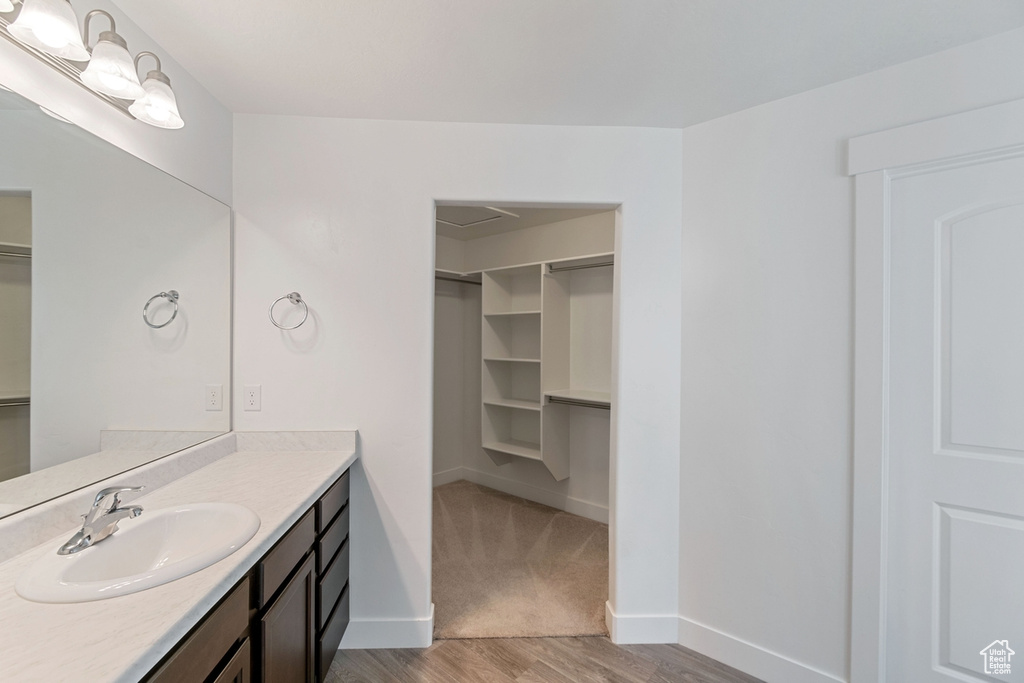 Bathroom featuring a walk in closet, vanity, and wood finished floors