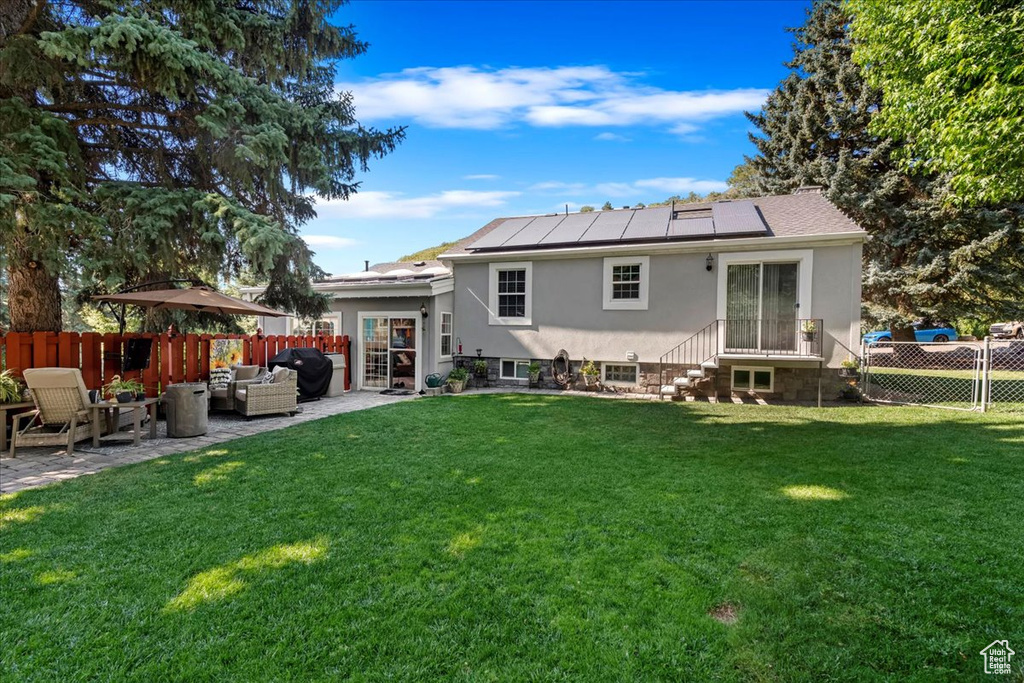 Rear view of house with an outdoor hangout area, stucco siding, roof mounted solar panels, and a patio