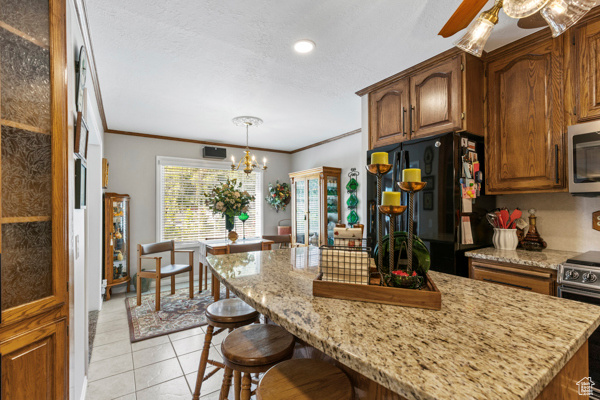 Kitchen with appliances with stainless steel finishes, a kitchen breakfast bar, crown molding, light tile patterned floors, and a ceiling fan