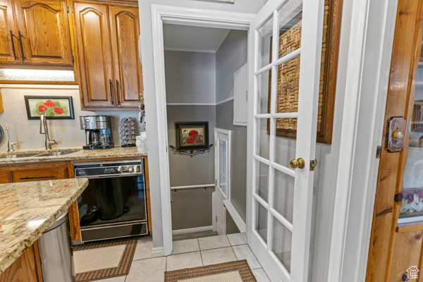 Kitchen with dishwasher, light stone countertops, brown cabinetry, light tile patterned flooring, and crown molding