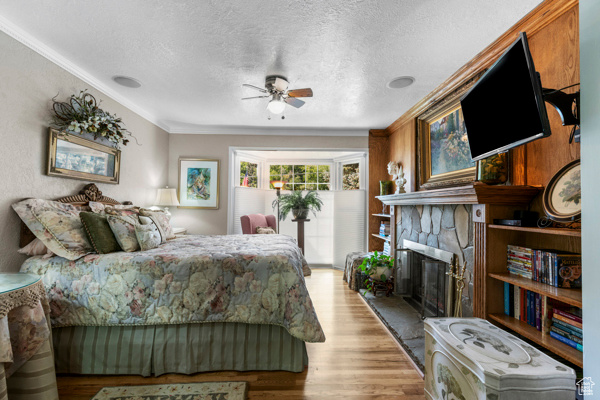 Bedroom featuring wood finished floors, a fireplace, a textured ceiling, crown molding, and ceiling fan