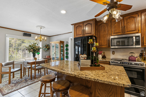 Kitchen with black appliances, a kitchen bar, light tile patterned flooring, light stone countertops, and a chandelier