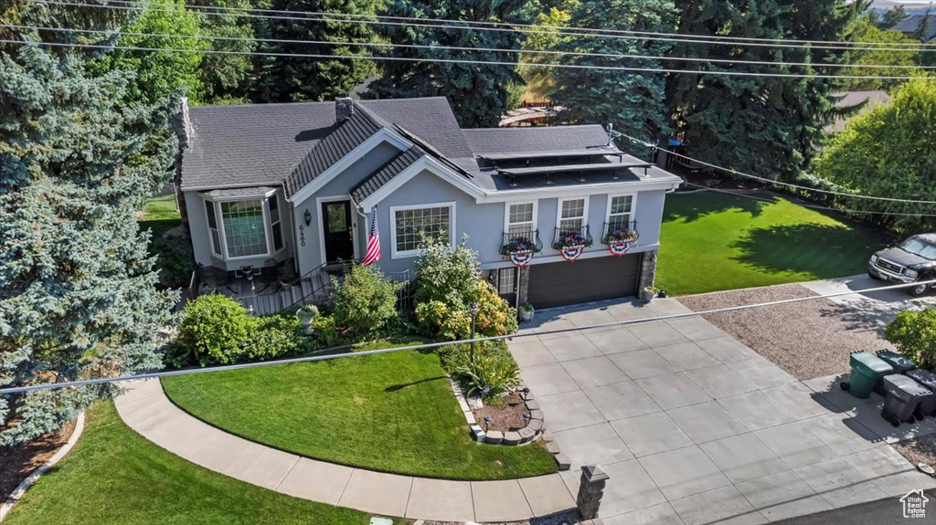 View of front of house featuring a garage, concrete driveway, stucco siding, roof mounted solar panels, and a front lawn
