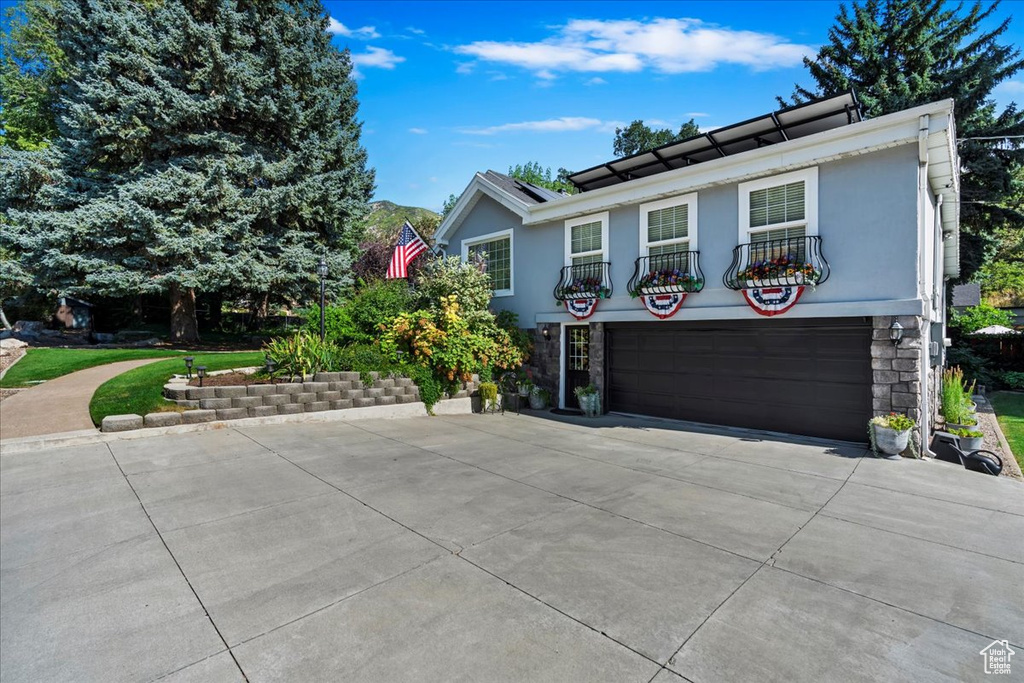 View of front of property featuring an attached garage, a balcony, concrete driveway, stucco siding, and stone siding