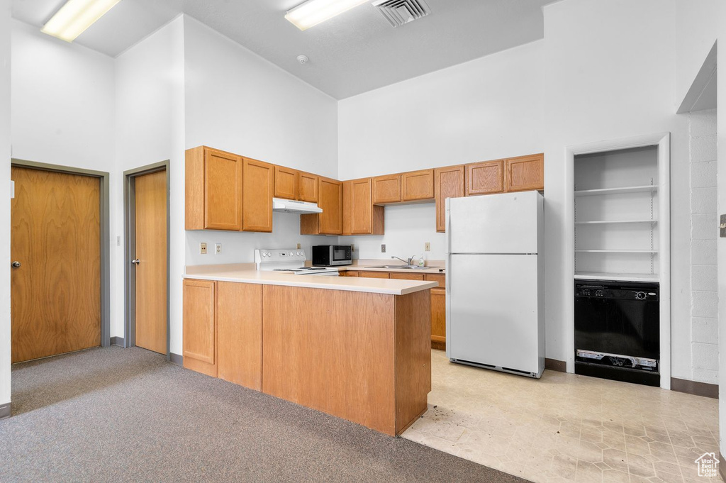 Kitchen with white appliances, a towering ceiling, light countertops, under cabinet range hood, and a peninsula