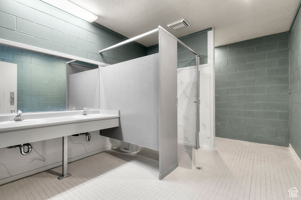 Full bath featuring walk in shower, tile patterned flooring, and concrete block wall