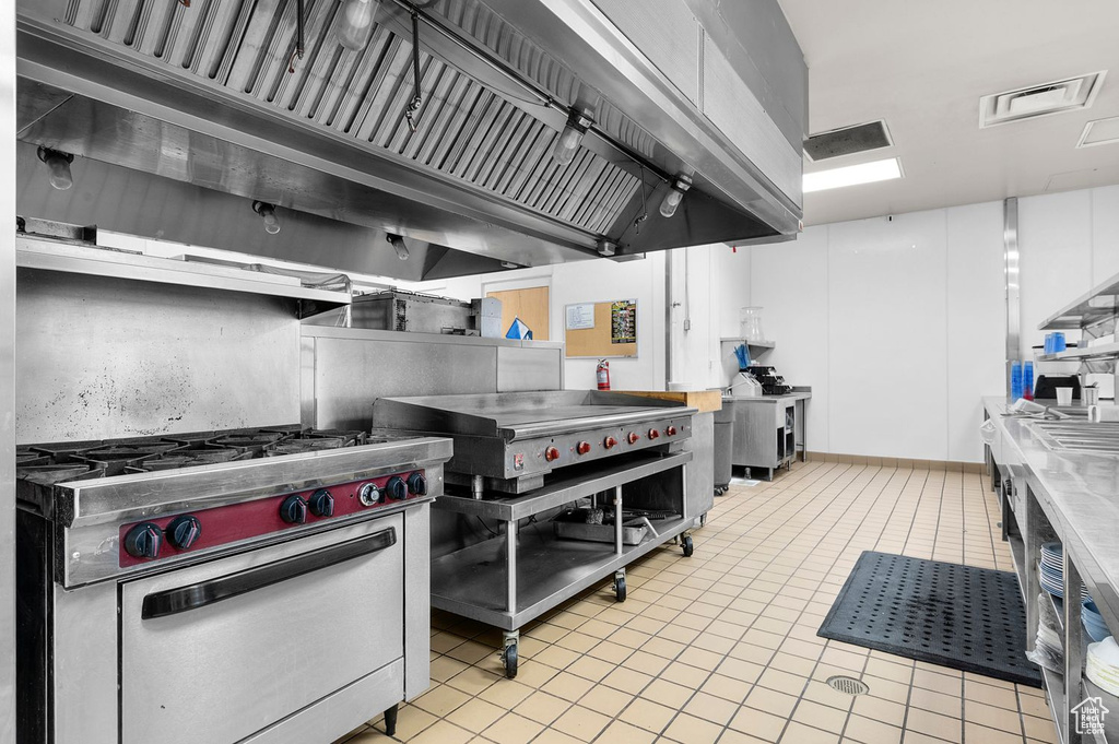 Kitchen with gas range, premium range hood, light tile patterned floors, and white cabinetry
