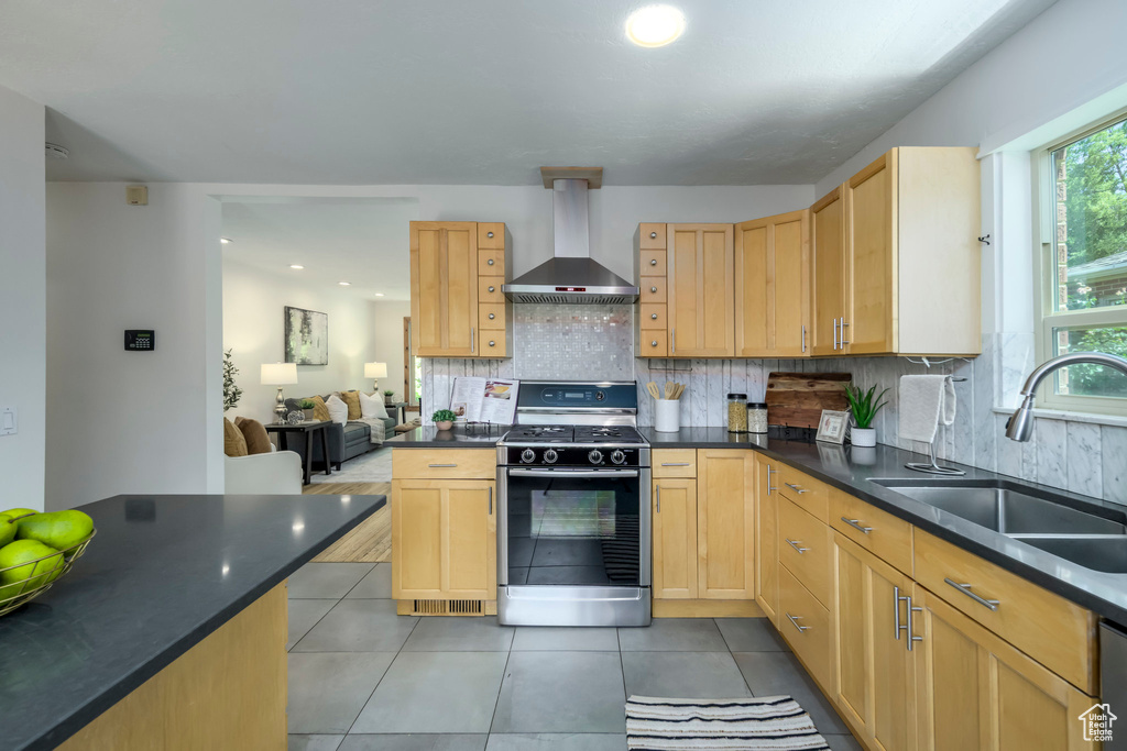 Kitchen featuring stainless steel gas range oven, wall chimney exhaust hood, dark countertops, light tile patterned floors, and recessed lighting