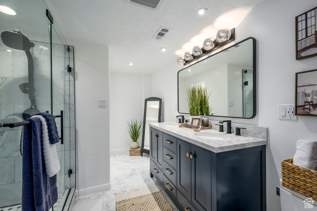 Full bath with marble look tiles, double vanity, a shower stall, and recessed lighting