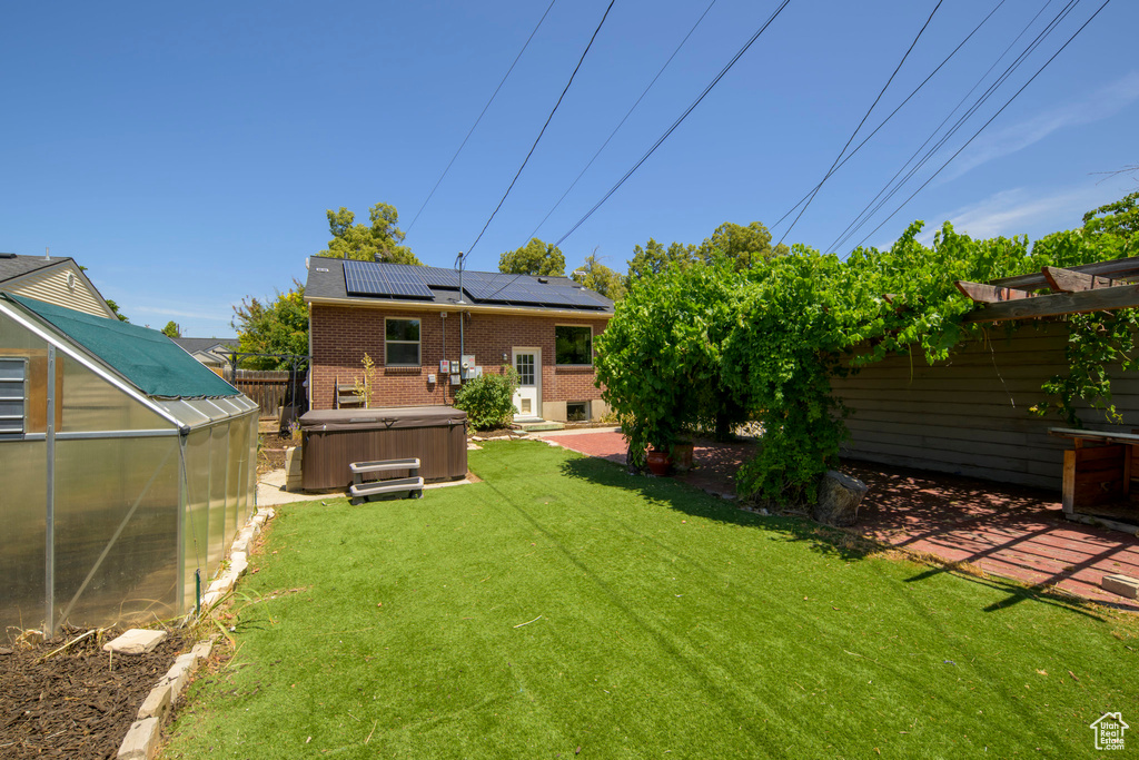 Fenced backyard with a hot tub, a greenhouse, an outbuilding, and a patio area