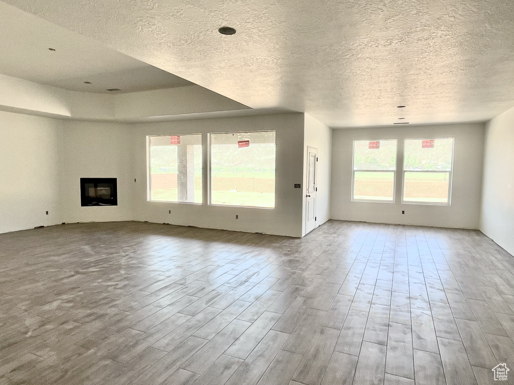 Unfurnished living room with a textured ceiling, plenty of natural light, wood finished floors, and a glass covered fireplace
