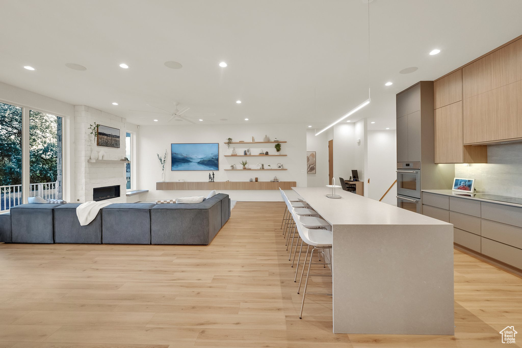 Kitchen featuring modern cabinets, light wood-type flooring, open floor plan, a large fireplace, and recessed lighting