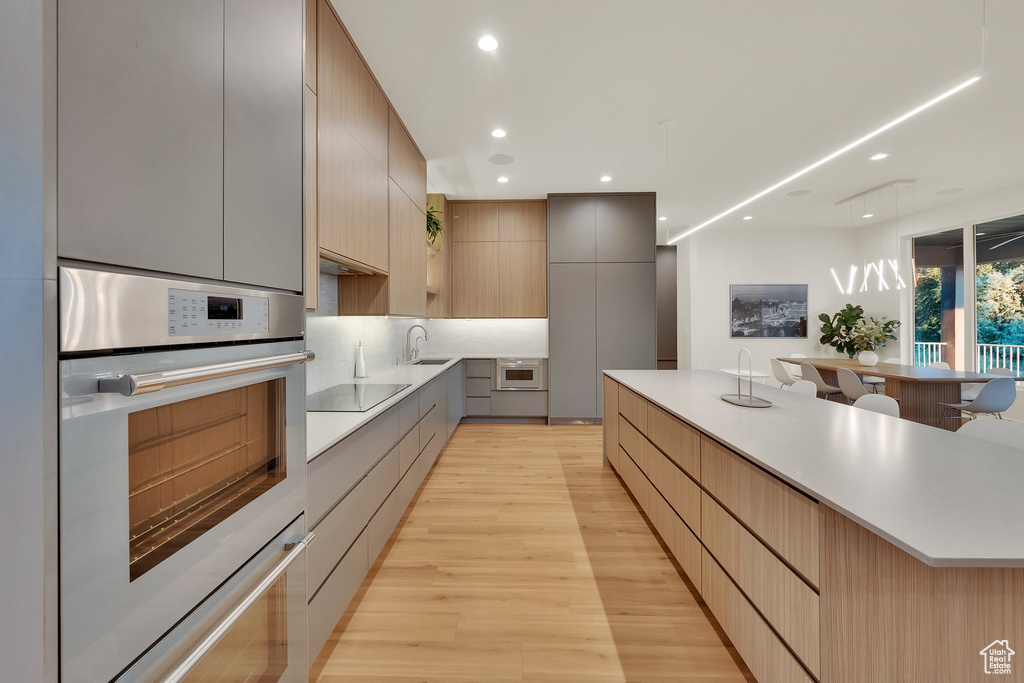 Kitchen with modern cabinets, light wood-style floors, double oven, light countertops, and black electric stovetop