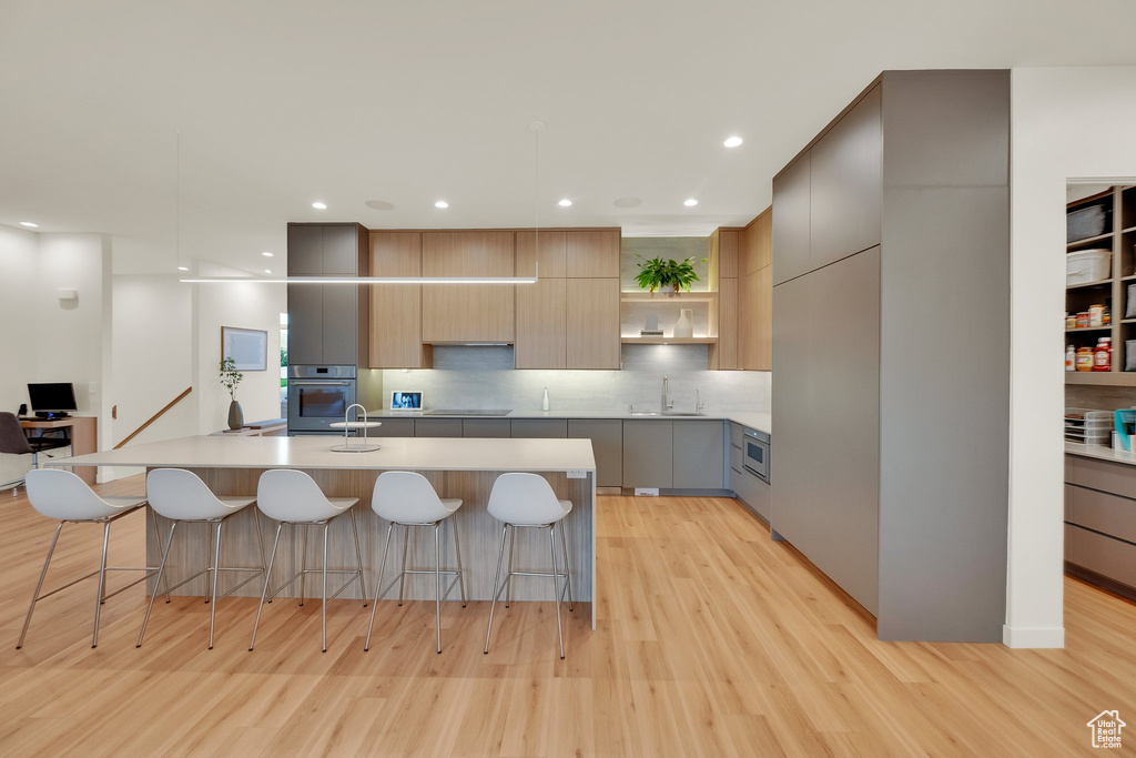 Kitchen with modern cabinets, stainless steel oven, open shelves, light wood finished floors, and gray cabinets