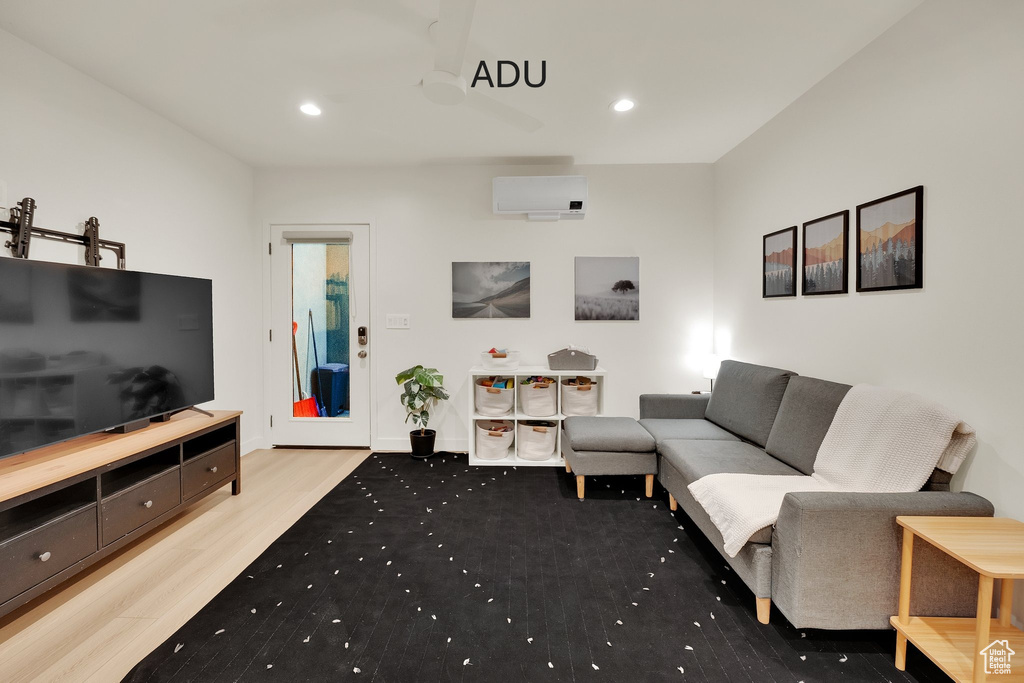 Living area with wood finished floors, a wall mounted AC, and recessed lighting