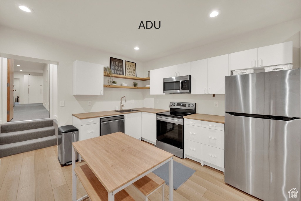 Kitchen featuring stainless steel appliances, open shelves, light wood-style flooring, white cabinets, and recessed lighting