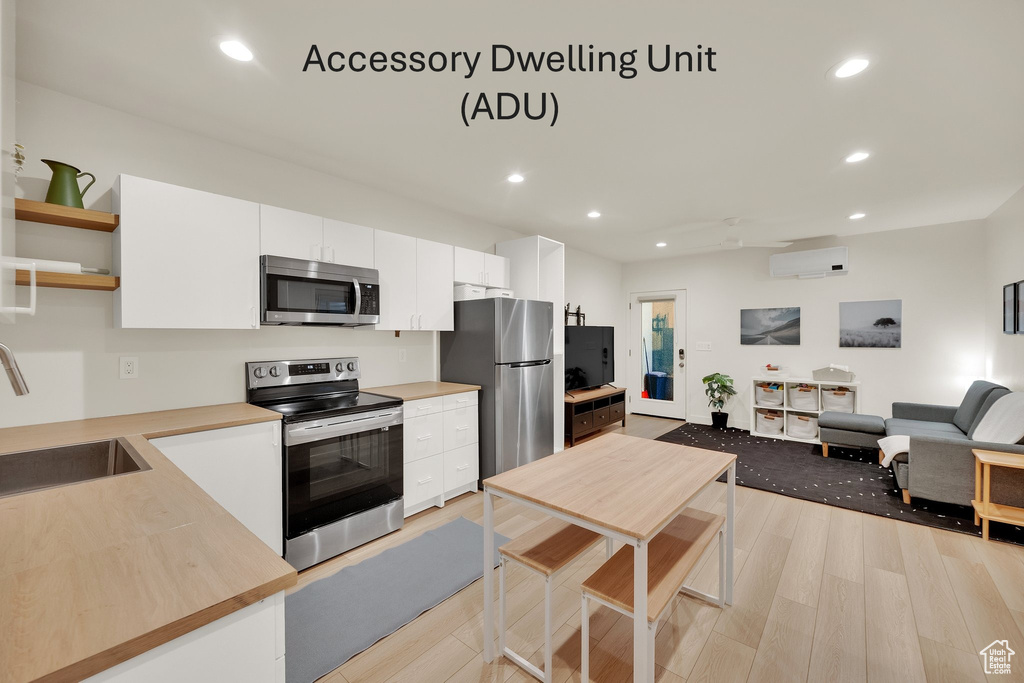 Kitchen with appliances with stainless steel finishes, open shelves, recessed lighting, light wood finished floors, and white cabinetry