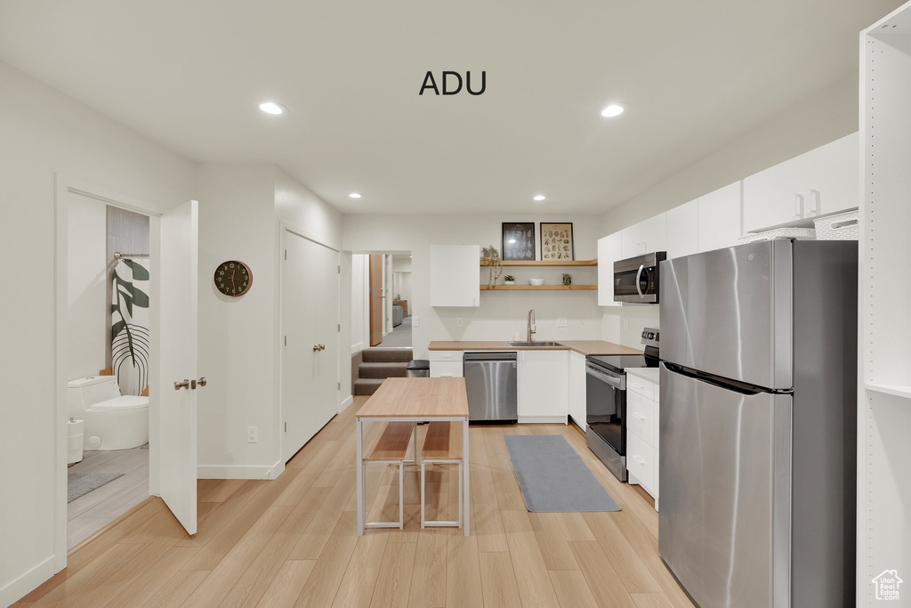 Kitchen featuring stainless steel appliances, open shelves, white cabinets, recessed lighting, and light wood-type flooring