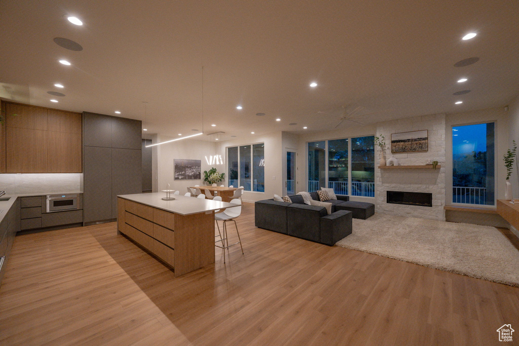 Kitchen with modern cabinets, light wood-style flooring, open floor plan, a large island, and a stone fireplace