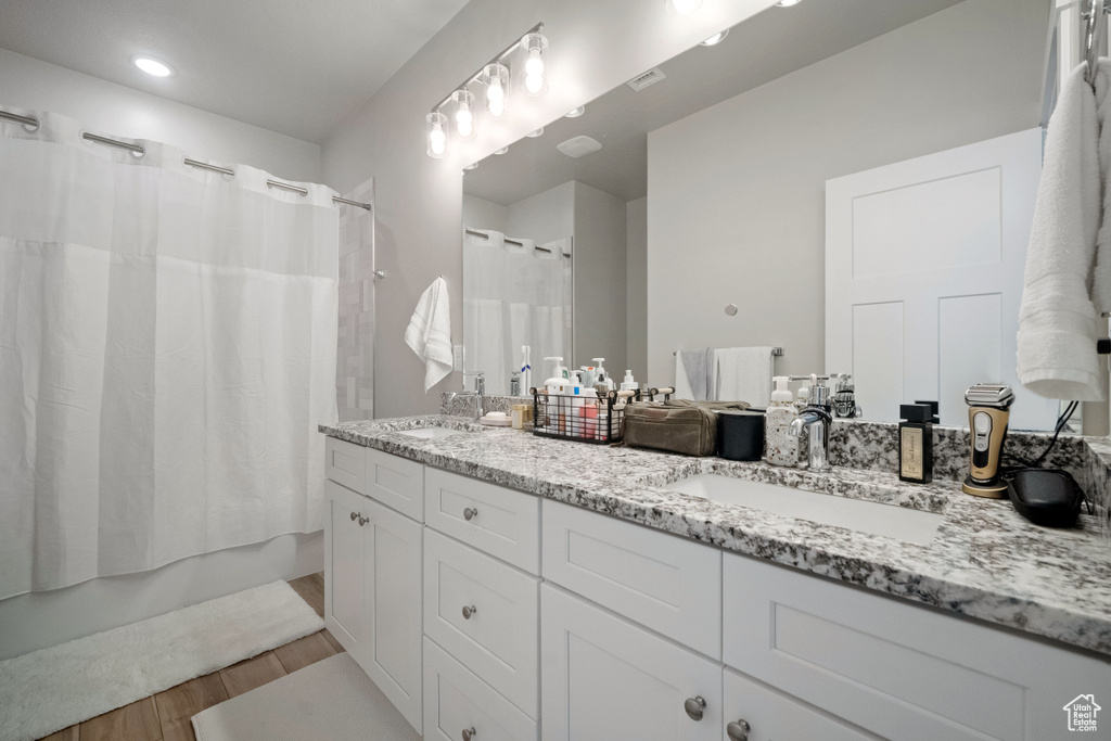 Full bathroom featuring double vanity, wood finished floors, and shower / tub combo