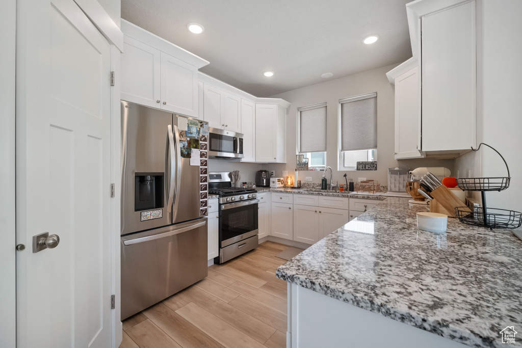 Kitchen with stainless steel appliances, white cabinets, light stone countertops, light wood-type flooring, and recessed lighting