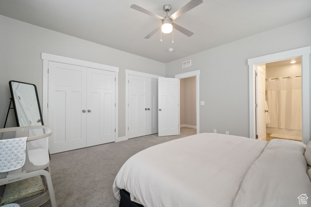 Bedroom featuring two closets, light colored carpet, connected bathroom, and ceiling fan
