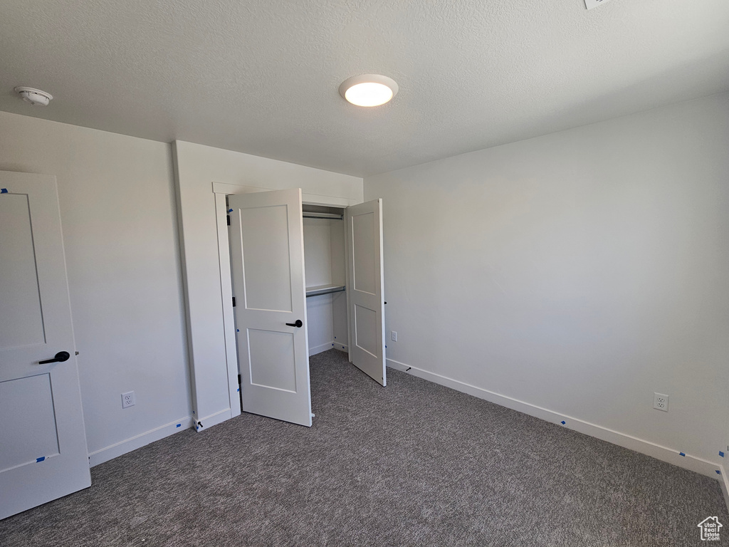 Unfurnished bedroom with dark carpet, a closet, and a textured ceiling