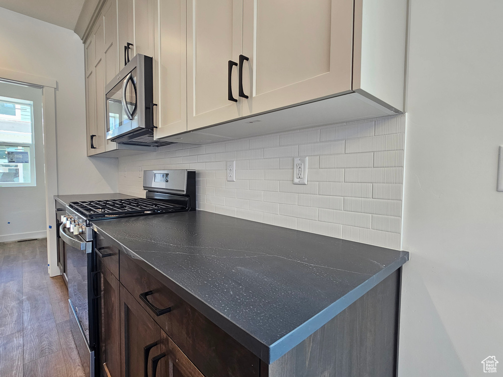 Kitchen featuring stainless steel appliances, decorative backsplash, dark countertops, and wood finished floors