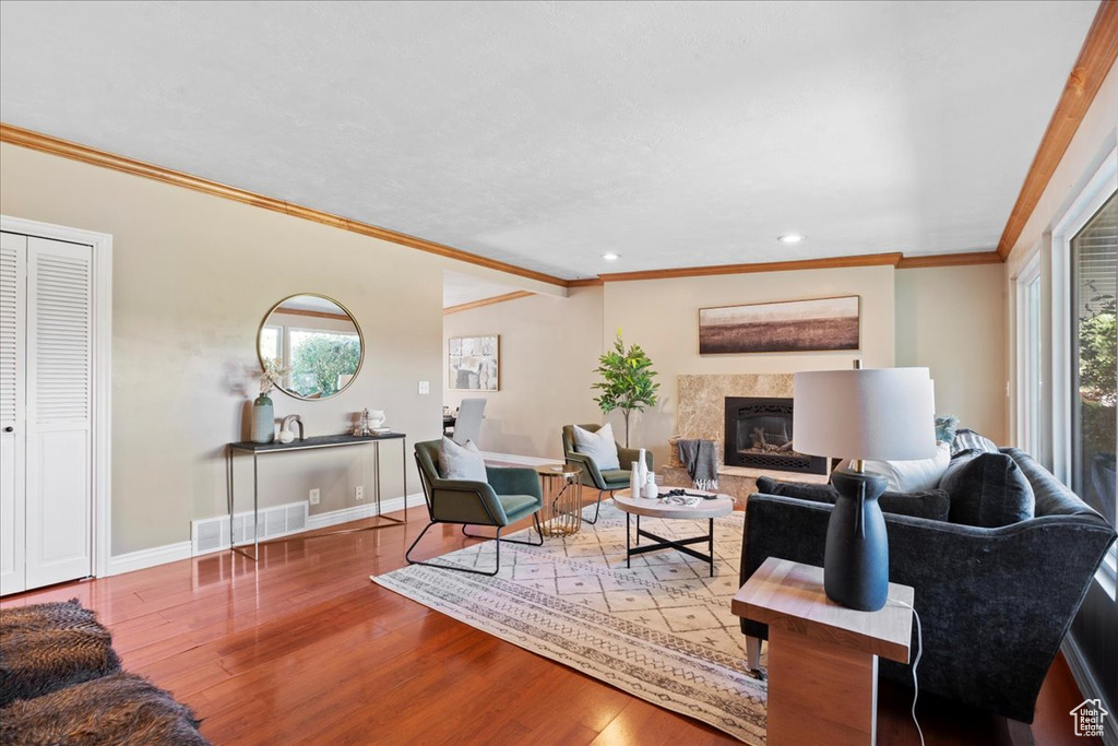 Living room with wood finished floors, a high end fireplace, crown molding, and recessed lighting
