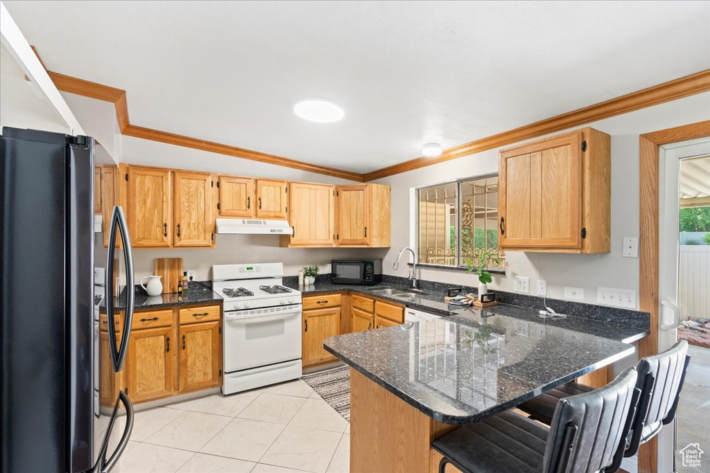 Kitchen featuring white gas stove, freestanding refrigerator, under cabinet range hood, crown molding, and a peninsula