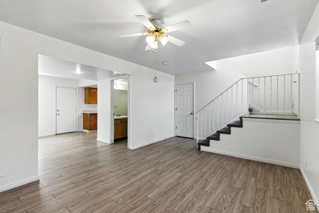 Unfurnished living room with wood finished floors, ceiling fan, and stairway