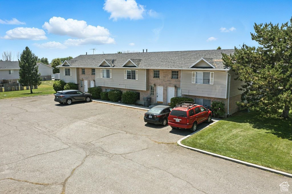 Bi-level home with brick siding, uncovered parking, a front lawn, and roof with shingles