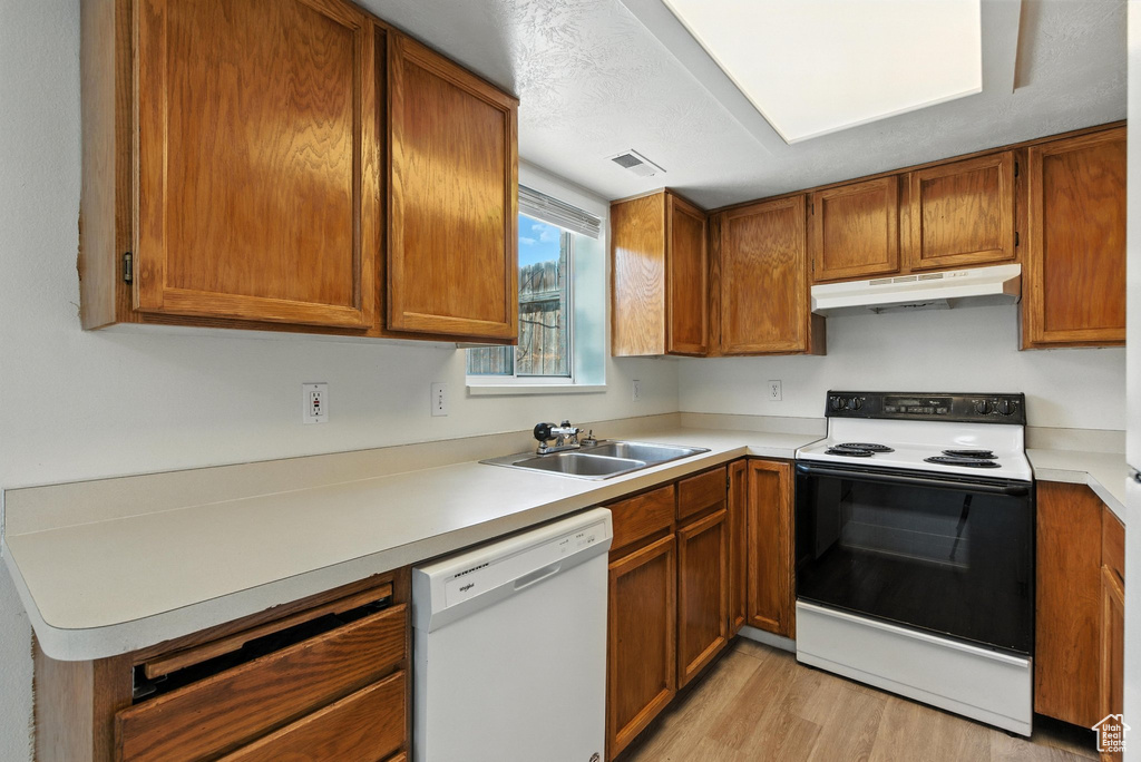 Kitchen featuring white appliances, under cabinet range hood, light wood-style flooring, and brown cabinets