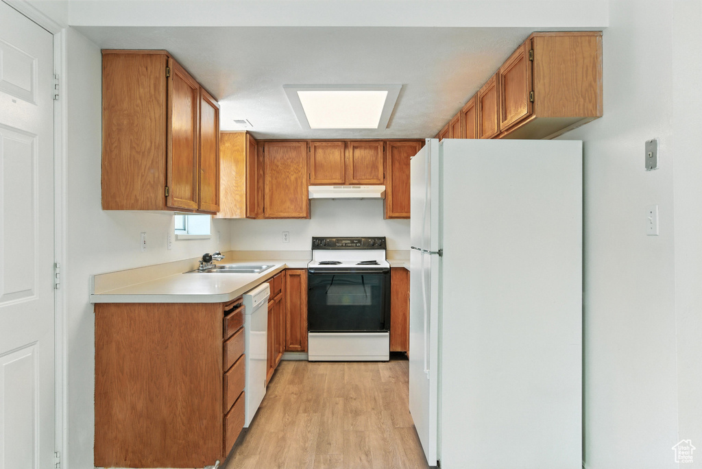 Kitchen featuring white appliances, under cabinet range hood, light wood-style floors, brown cabinetry, and light countertops