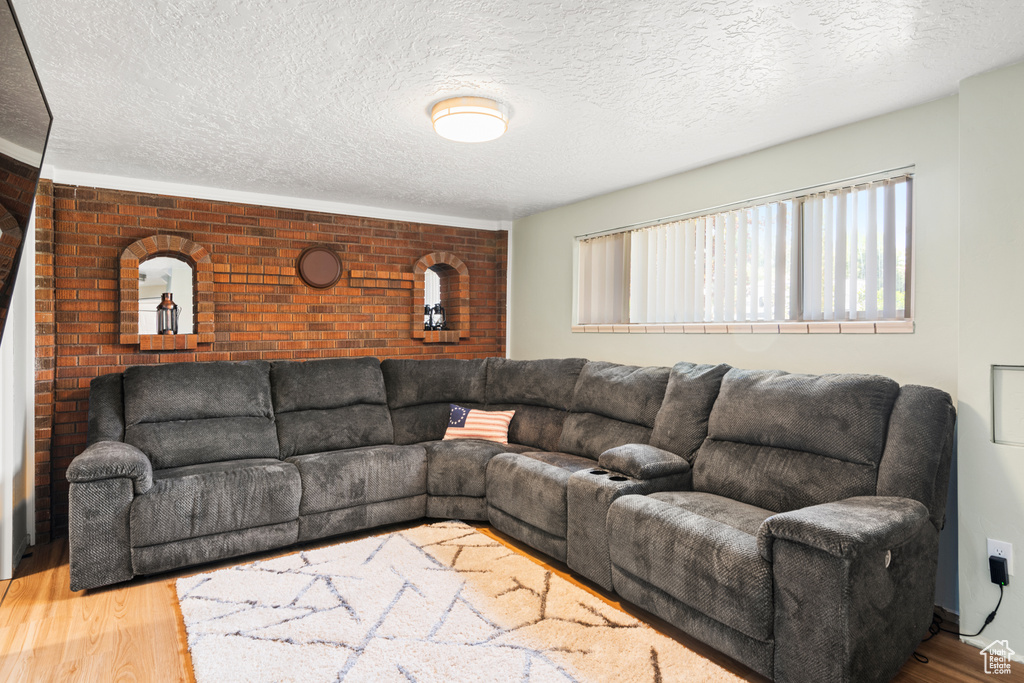 Living area with brick wall, wood finished floors, a textured ceiling, and an accent wall