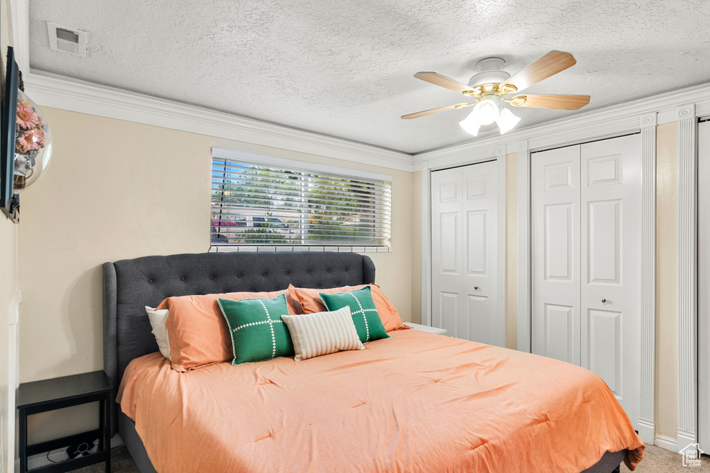 Bedroom featuring two closets, crown molding, a textured ceiling, a ceiling fan, and carpet