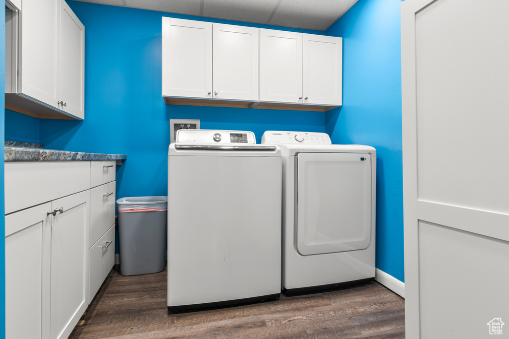 Laundry room with washing machine and clothes dryer, cabinet space, and wood finished floors