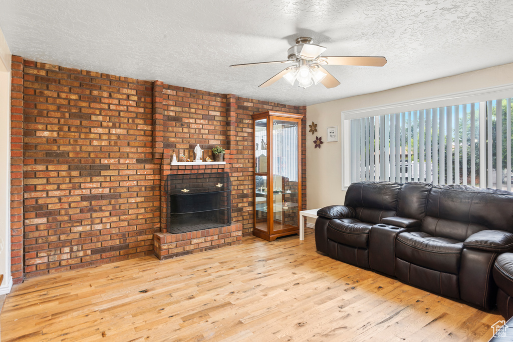 Living area with wood finished floors, a textured ceiling, ceiling fan, a fireplace, and brick wall