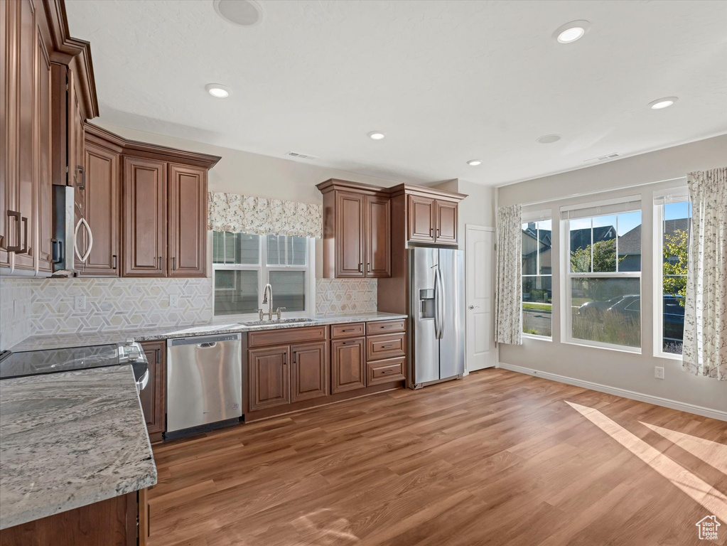 Kitchen featuring appliances with stainless steel finishes, light wood-style floors, tasteful backsplash, recessed lighting, and light stone countertops