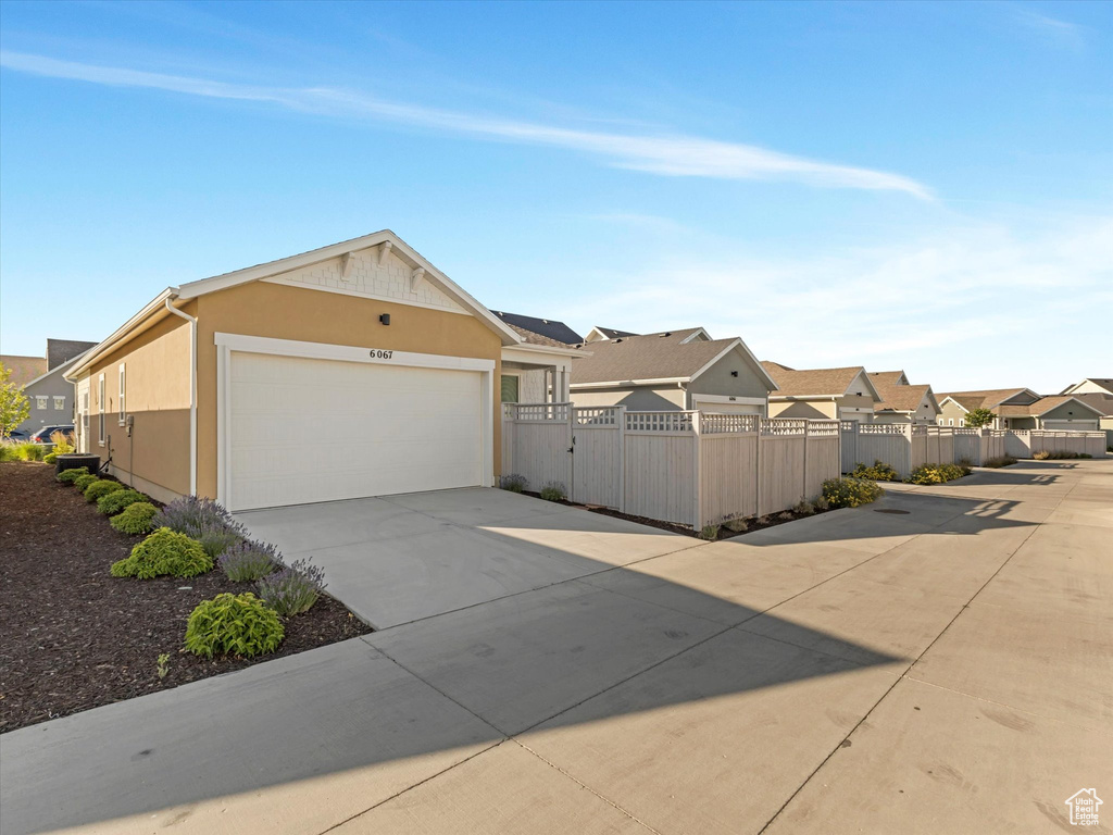View of side of property featuring concrete driveway, a residential view, stucco siding, an attached garage, and a gate