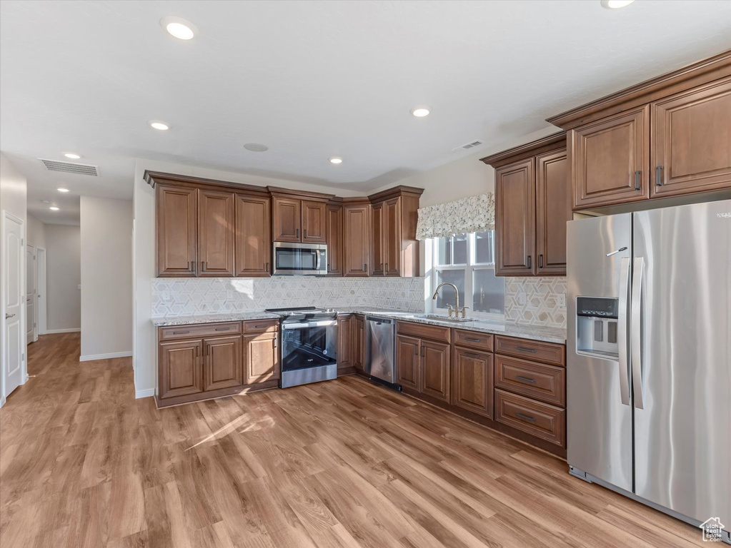 Kitchen featuring appliances with stainless steel finishes, light stone counters, light wood finished floors, tasteful backsplash, and recessed lighting