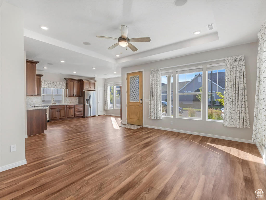 Unfurnished living room featuring a tray ceiling, a ceiling fan, dark wood-style flooring, and recessed lighting