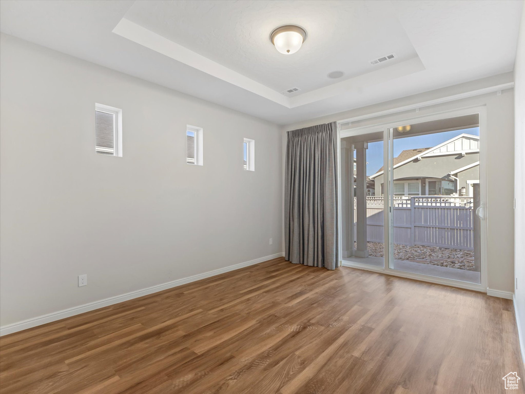 Unfurnished room featuring a tray ceiling, wood finished floors, and healthy amount of natural light