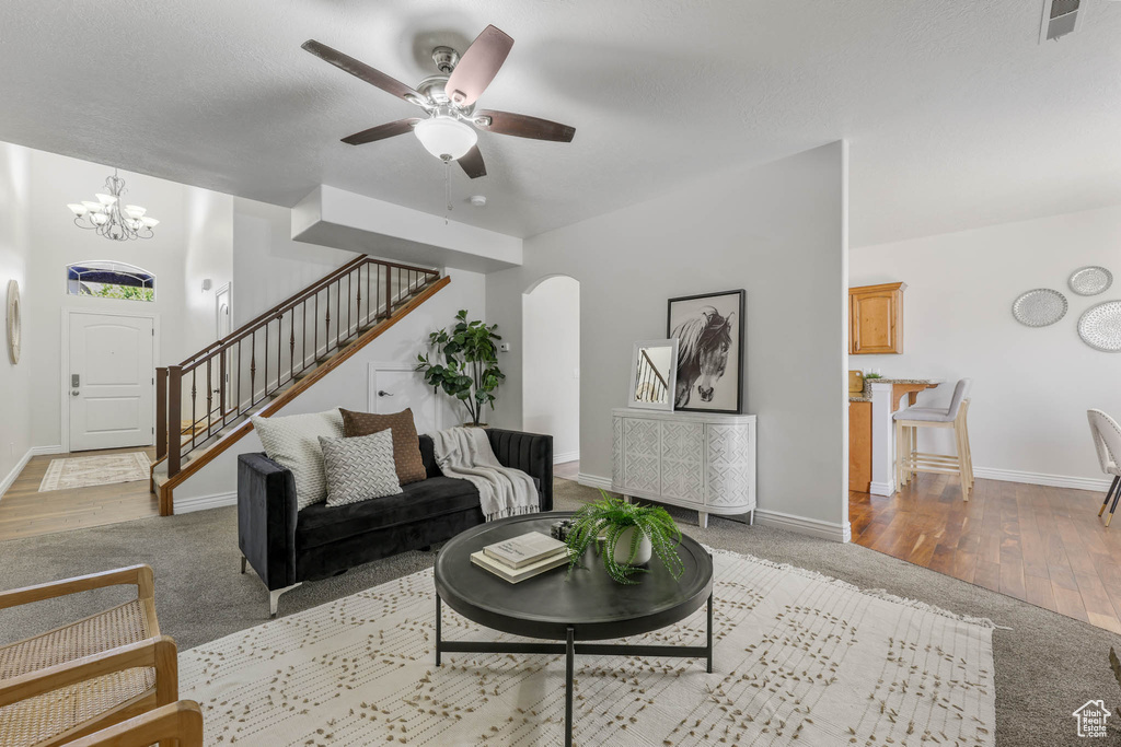 Carpeted living room with arched walkways, stairway, a chandelier, ceiling fan, and wood finished floors