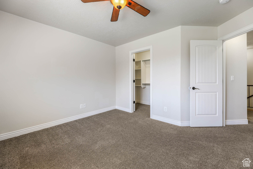Unfurnished bedroom with carpet, a walk in closet, a closet, and a ceiling fan