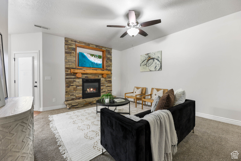 Living area featuring ceiling fan, carpet, and a stone fireplace