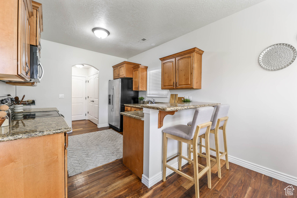 Kitchen featuring arched walkways, stainless steel fridge with ice dispenser, stone counters, a kitchen breakfast bar, and a textured ceiling