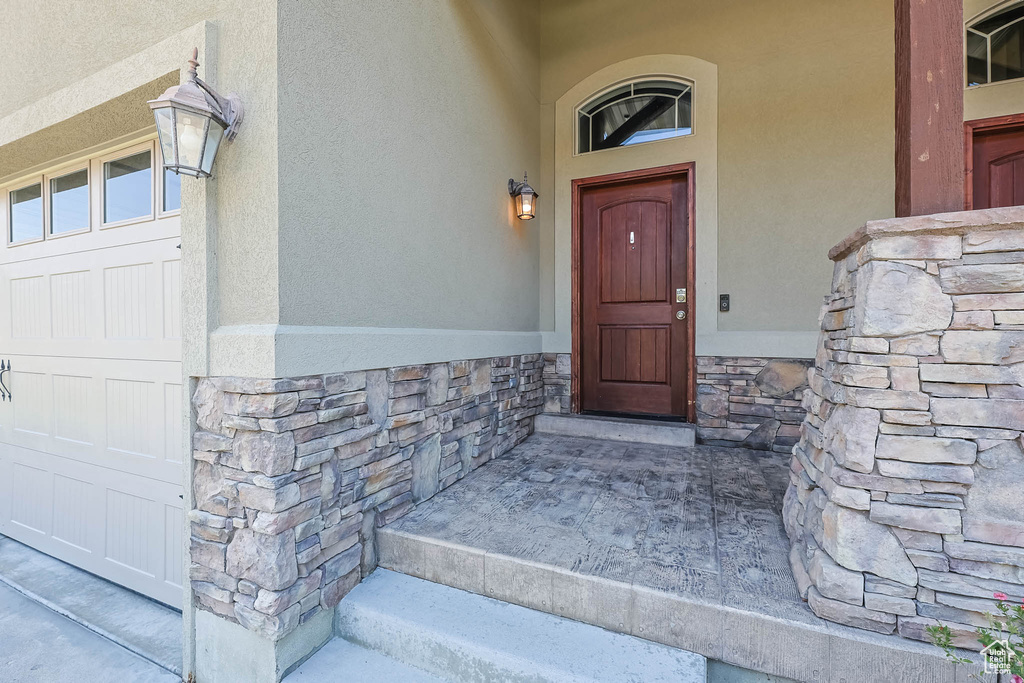 Doorway to property with stucco siding, stone siding, and a garage