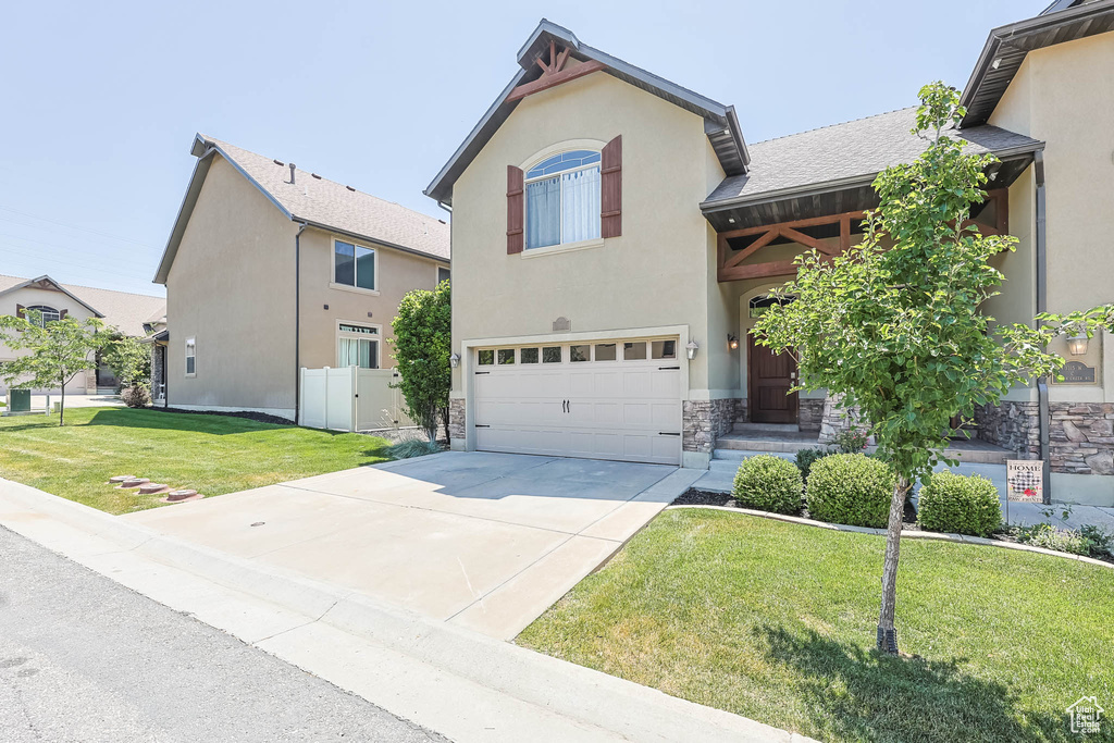 View of front of property featuring an attached garage, driveway, stone siding, and stucco siding